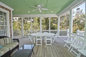 A covered porch with a white table and chairs, a striped sofa, and a ceiling fan. - Carolina, Oceanside House in Emerald Isle, NC! (Emerald Isle)