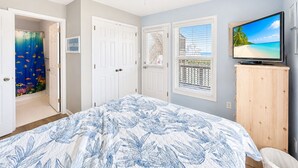 Une chambre à coucher avec un lit, un ventilateur de plafond, une télévision et une vue sur la plage par la fenêtre.