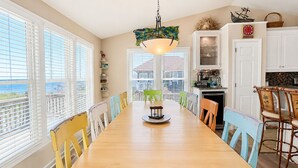 Un espace repas comprenant une table en bois, des chaises, un luminaire suspendu et une vue dégagée sur l’extérieur grâce à de grandes fenêtres.
