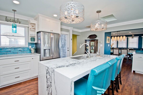 A modern kitchen with white cabinets, a marble island, and blue chairs.