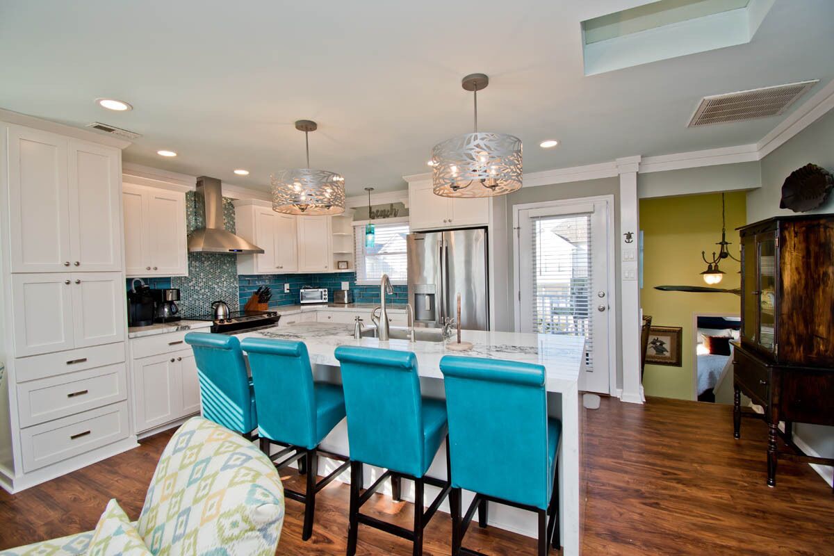 A modern kitchen with white cabinets, a central island with bar stools, and pendant lighting.