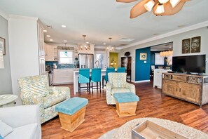 A spacious living area with a kitchen in the background, featuring a dining table with chairs, a sofa, and a television.