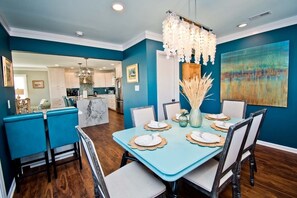 A dining area with a teal table, white chairs, and a chandelier. - Carolina Conch House, Almost Oceanfront House in Emerald Isle, NC! (Emerald Isle)