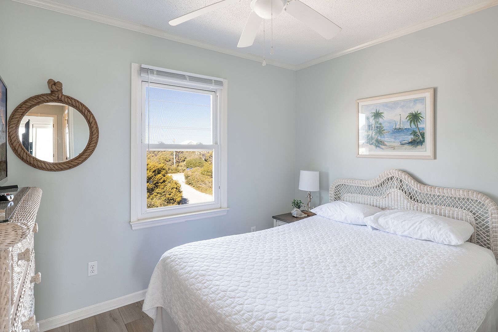 A bedroom with a large bed, a window with a view, a bedside table with a lamp, and a framed picture on the wall.