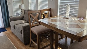 A cozy living room with a wooden dining table, a gray sofa, and a wooden chair. - SPACIOUS 1 BEDROOM LOFT IN DISNEY AREA 5 STAR RATED MILL CREEK RESORT 2767 (Kissimmee)