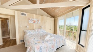 A bedroom with a bed, a window with blinds, a door, and a wall-mounted artwork. - Carousel, Oceanfront House in Emerald Isle, NC! (Emerald Isle)
