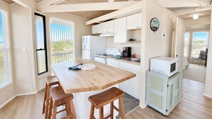 A compact kitchen with a wooden table, bar stools, a refrigerator, a stove, and a microwave. - Carousel, Oceanfront House in Emerald Isle, NC! (Emerald Isle)