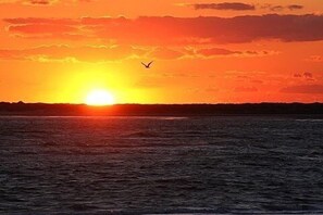 Solnedgang over vand, med silhuetten af land i det fjerne.
