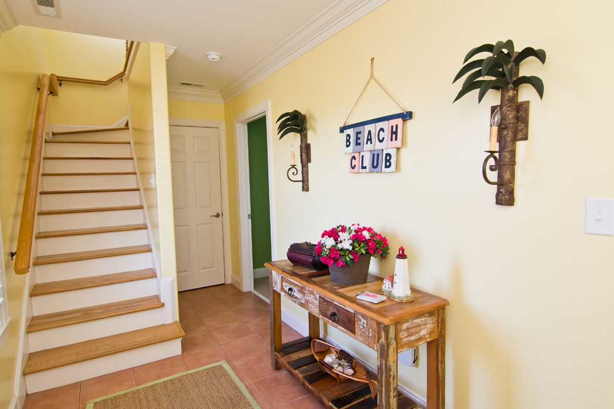 Una escala que porta a un espai amb una taula de consola de fusta, un rètol que diu 'BEACH CLUB' i una planta en test.