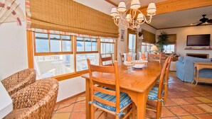 A spacious dining area with a wooden table and chairs, a chandelier, and large windows offering a view of the outdoors. - Casa Atlantica, Oceanfront House in Pine Knoll Shores, NC! (Pine Knoll Shores)