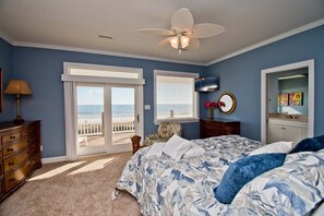 A bedroom with a bed, a dresser, a ceiling fan, a large window with blinds, and a view of the ocean. - Casa Bianco, Oceanfront House in Emerald Isle, NC! (Emerald Isle)
