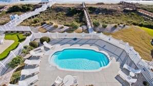 Zona de piscina con vista despejada al océano, rodeada de sillas de deck blancas y una terraza de madera.