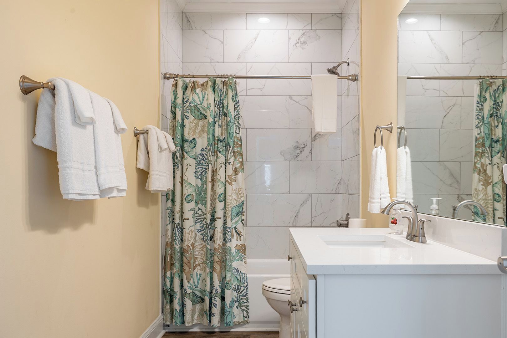 Un baño con cortina de ducha, inodoro, lavamanos con espejo y toallas colgadas en la pared.