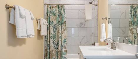 Un baño con cortina de ducha, inodoro, lavamanos con espejo y toallas colgadas en la pared.