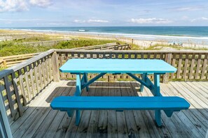 Une terrasse en bois avec une table et un banc de pique-nique turquoise, donnant sur une plage.