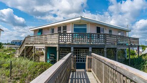 Une maison à deux étages avec un balcon, une terrasse en bois et une vue sur la plage.