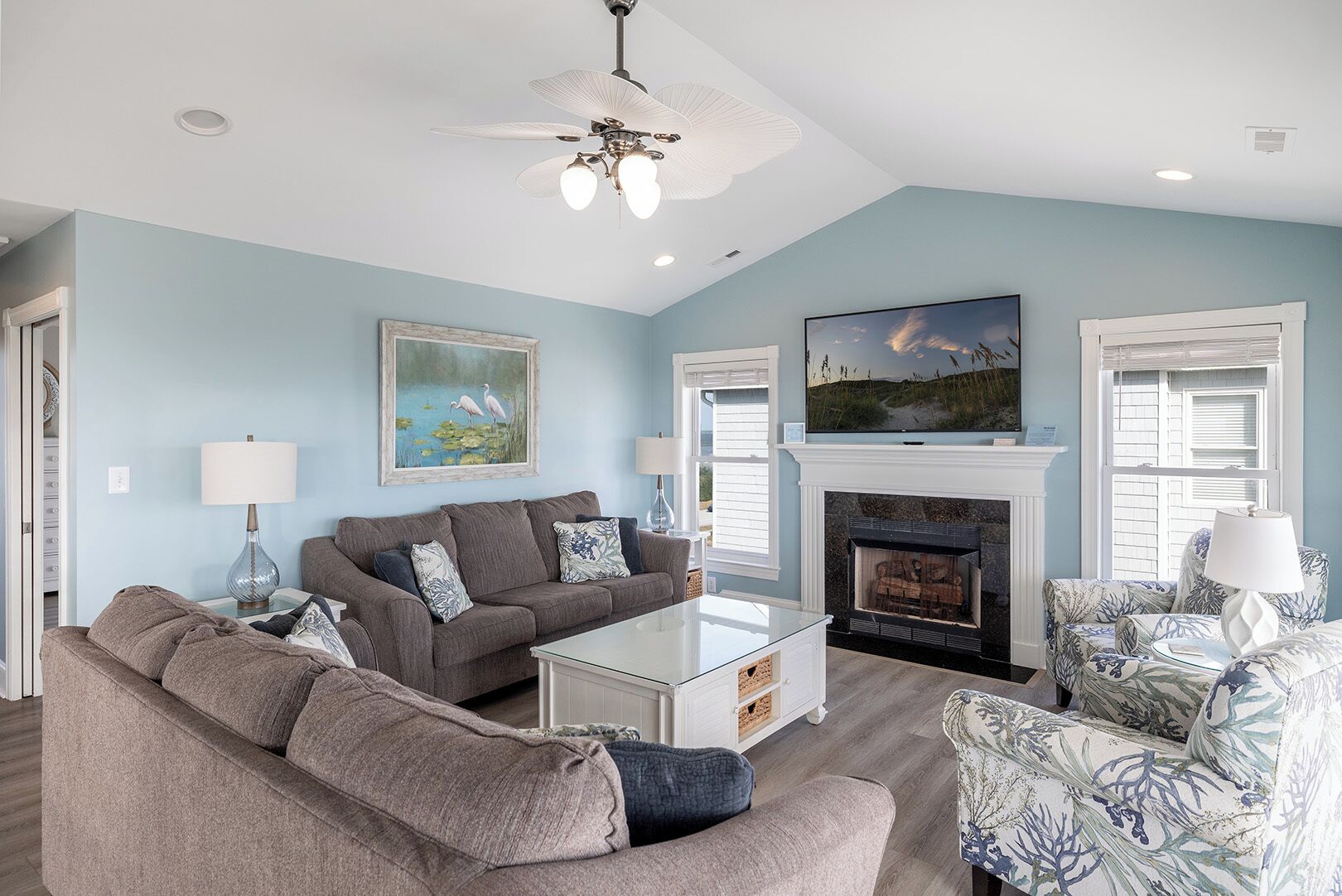 A living room with a fireplace, a ceiling fan, and a television mounted above it.