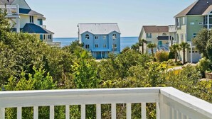A coastal residential area with houses, a clear view of the ocean, and a white railing in the foreground. - Chillin' The Most, Oceanview House in Emerald Isle, NC! (Emerald Isle)