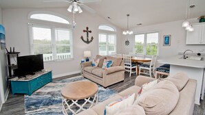 A spacious living area with a sofa, a coffee table, a TV, and a dining area with chairs and a table. - Chillin' The Most, Oceanview House in Emerald Isle, NC! (Emerald Isle)