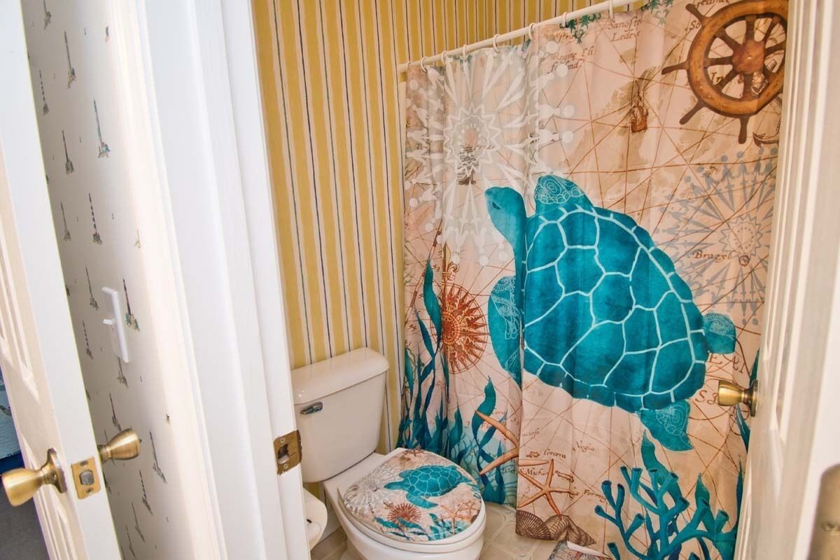Une salle de bain avec des toilettes, un rideau de douche orné d’un motif de tortue de mer et un mur à rayures.