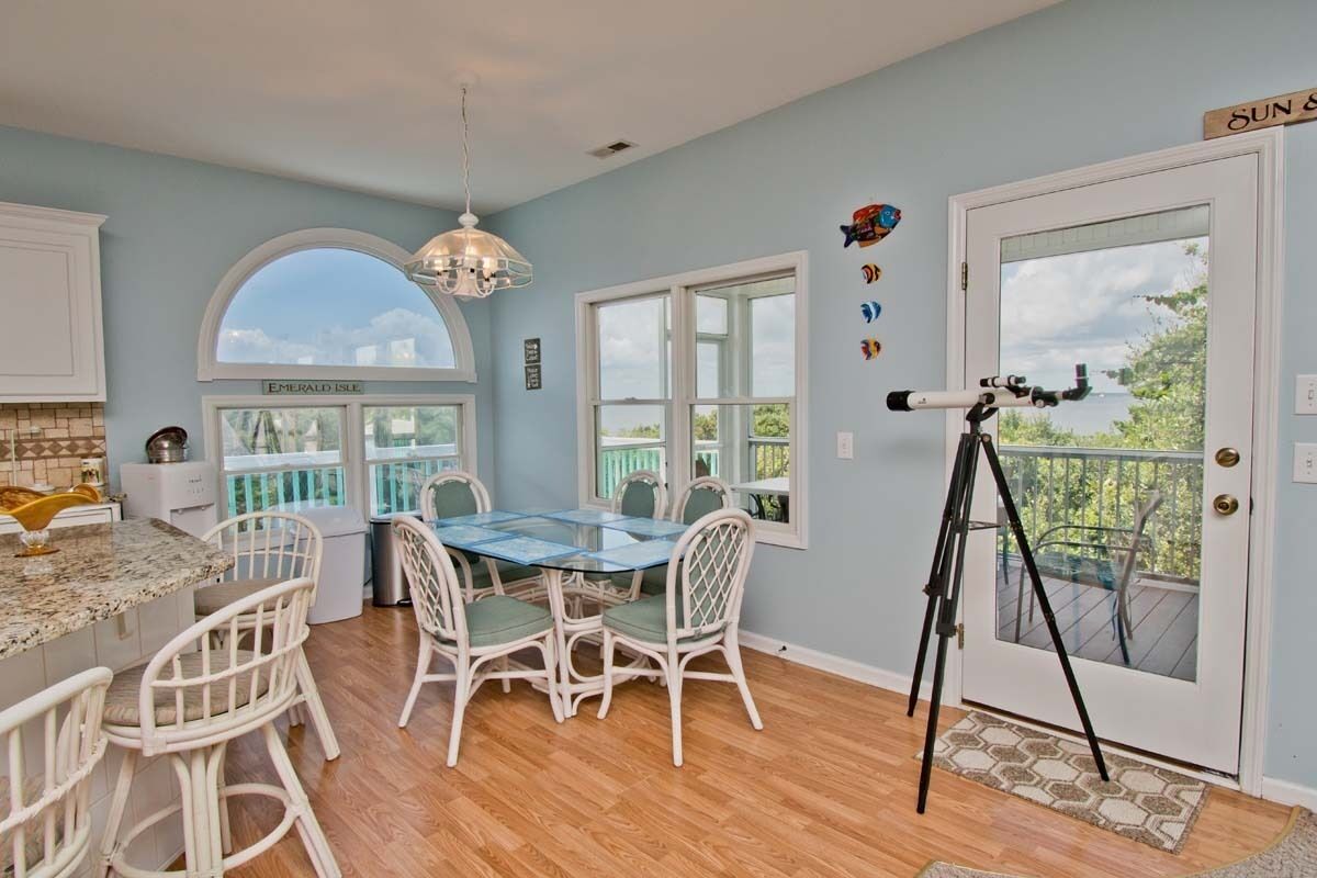 A kitchen with a dining table, chairs, a chandelier, and a telescope on a balcony.