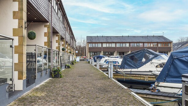 A narrow brick pathway leading to a row of boats, flanked by buildings with a mix of modern and traditional architecture. - 2 bedroom accommodation in Carnforth (Carnforth)