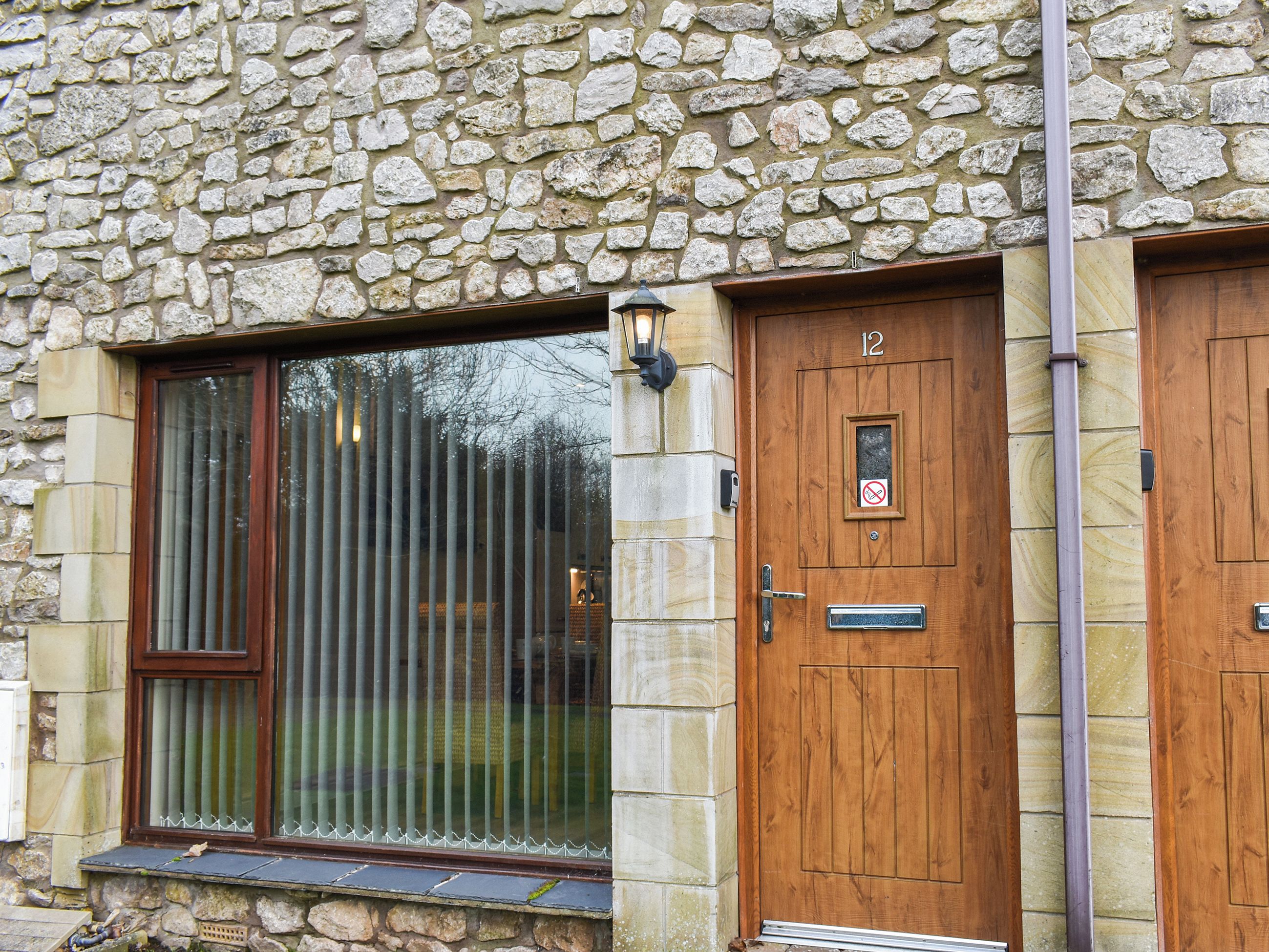 A stone facade with a wooden door marked '12' and a window with vertical blinds.