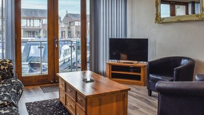 A room with a wooden TV stand, a leather sofa, a large mirror, and a view through a sliding glass door. - 2 bedroom accommodation in Carnforth (Carnforth)