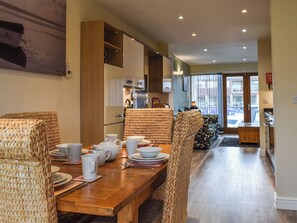 A dining area with a wooden table set for four, wicker chairs, and a kitchen in the background.