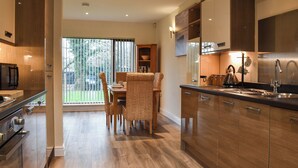 A modern kitchen with wooden cabinets, a dining area with wicker chairs, and a large window with a view of greenery. - 2 bedroom accommodation in Carnforth (Carnforth)