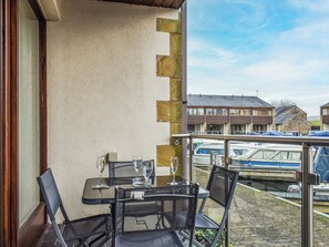 Un balcón con mesa y sillas, vistas a casas y un muelle para barcos.