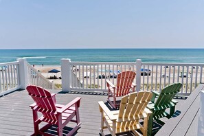A deck with Adirondack chairs overlooking a beach with umbrellas and people.
