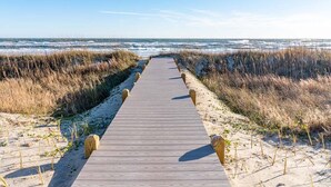 A wooden boardwalk leading to the beach, surrounded by sand and tall grasses. - Compass Pointe, Oceanfront House in Emerald Isle, NC! (Emerald Isle)
