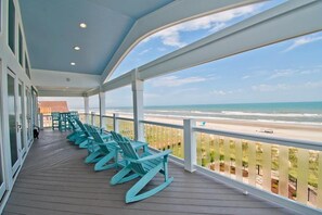 A covered deck with rocking chairs overlooking a beach. - Compass Pointe, Oceanfront House in Emerald Isle, NC! (Emerald Isle)