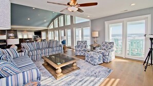 A spacious living room with striped sofas, a coffee table, and a ceiling fan. - Compass Pointe, Oceanfront House in Emerald Isle, NC! (Emerald Isle)
