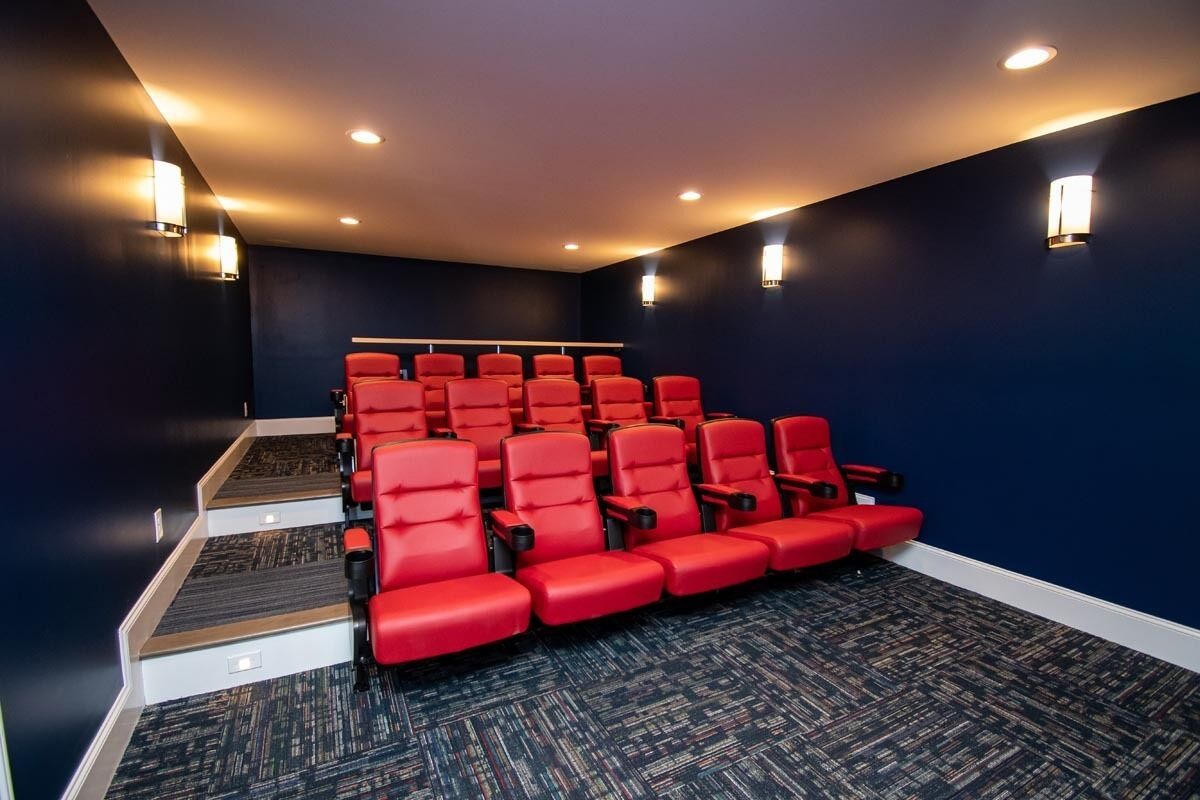 A theater with rows of red seats, carpeted floor, and wall sconces.