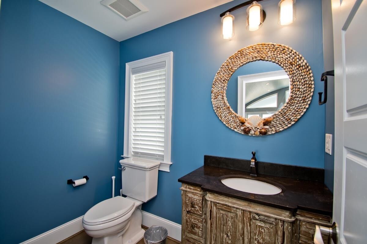 A bathroom with a blue wall, white toilet, and a wooden vanity with a round mirror.