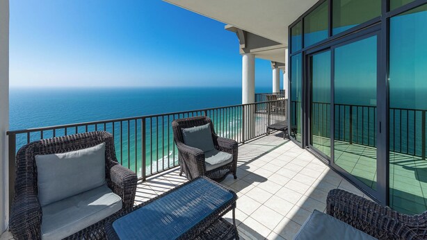 A balcony with wicker furniture, a glass door, and a view of the ocean.