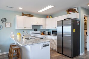 A modern kitchen with white cabinets, a stainless steel refrigerator, a built-in oven, and a marble countertop.