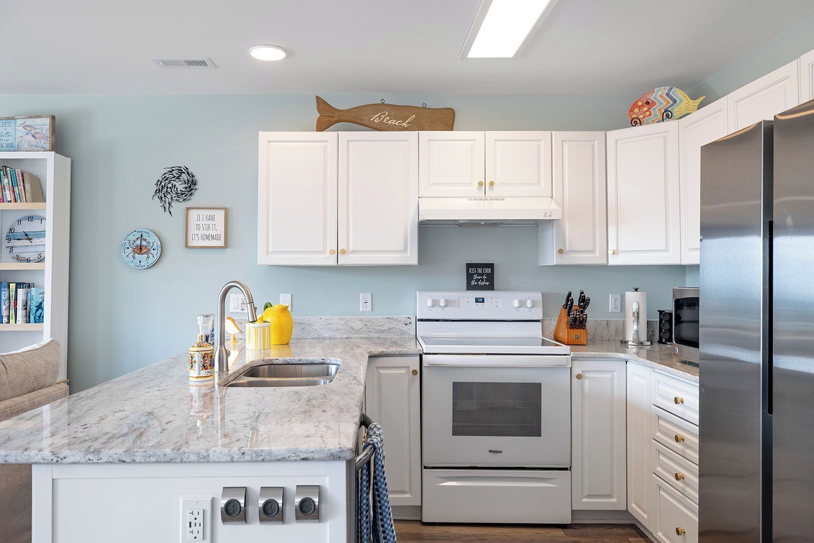 A modern kitchen with white cabinets, a stainless steel refrigerator, a built-in oven, and a marble countertop.