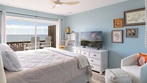 Een slaapkamer met een groot bed, een televisie, een dressoir en uitzicht op de oceaan.