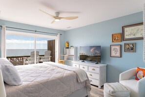 A bedroom with a large bed, a TV, a dresser, and a view of the ocean.
