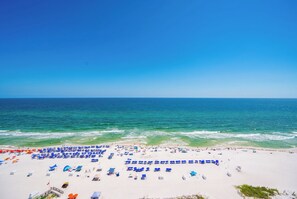 A beach with rows of sun loungers and umbrellas, a clear blue sky, and the ocean in the background.
