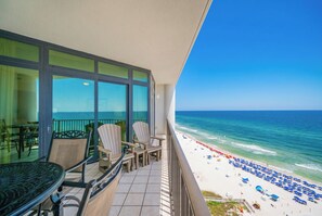 A balcony with a view of the beach, a table, chairs, and a railing.