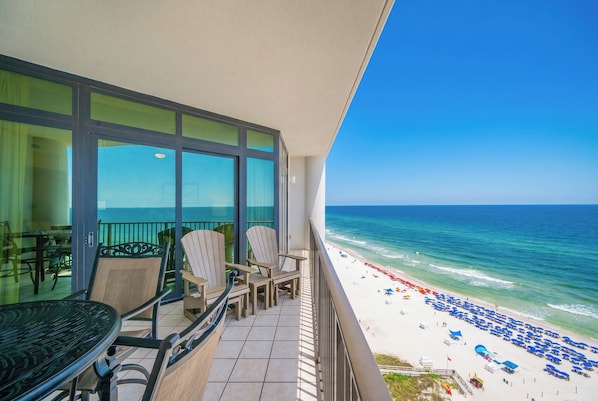 A balcony with a view of the beach, a table, chairs, and a railing.