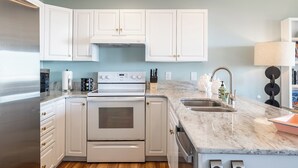 A kitchen with white cabinets, a stainless steel refrigerator, a built-in oven, and a marble countertop. - Angel's at the Pier West - Oceanfront Duplex in Emerald Isle, NC! (Emerald Isle)