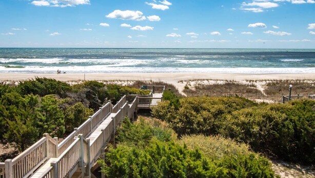 A beach with a wooden boardwalk leading to the shore, surrounded by dense greenery. - Angel's at the Pier West - Oceanfront Duplex in Emerald Isle, NC! (Emerald Isle)
