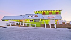 Un edificio verde con un letrero que dice "Surf's Up! Bar" y "Bogue Island Inn". Cuenta con una escalera que lleva a la entrada y una valla de madera al frente.