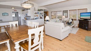 Uma sala de estar ampla com uma mesa de jantar de madeira, sofás brancos e uma televisão.