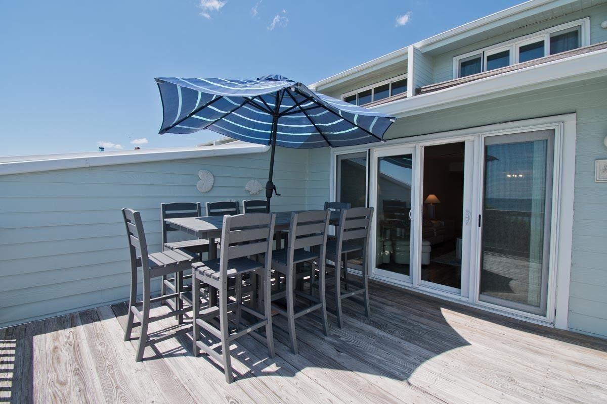 En terrasse med et bord, stole, en parasol og en skydedør, der fører til et indre rum.